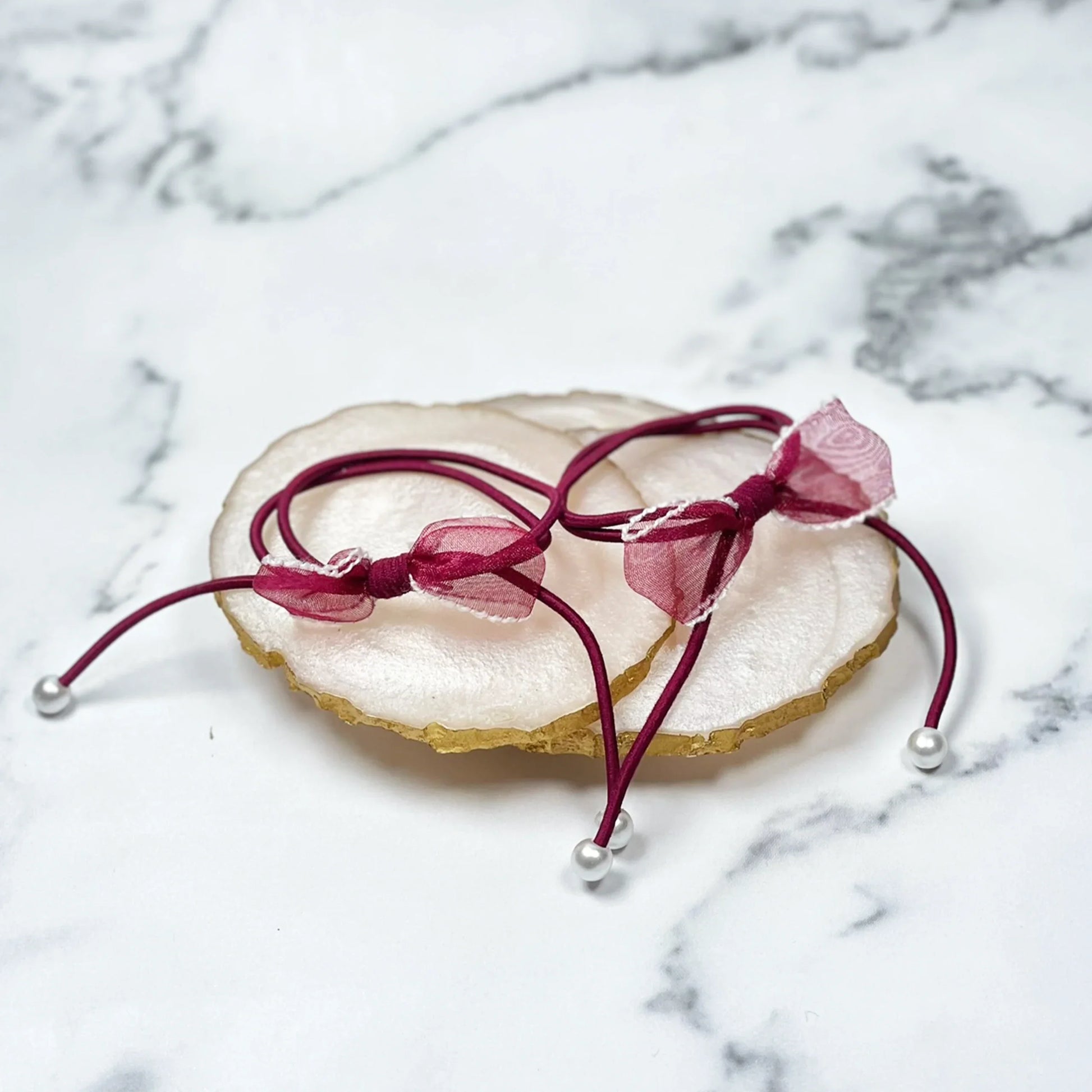 Burgundy hair ties with bows and beads placed on white marble surface with decorative stone tray