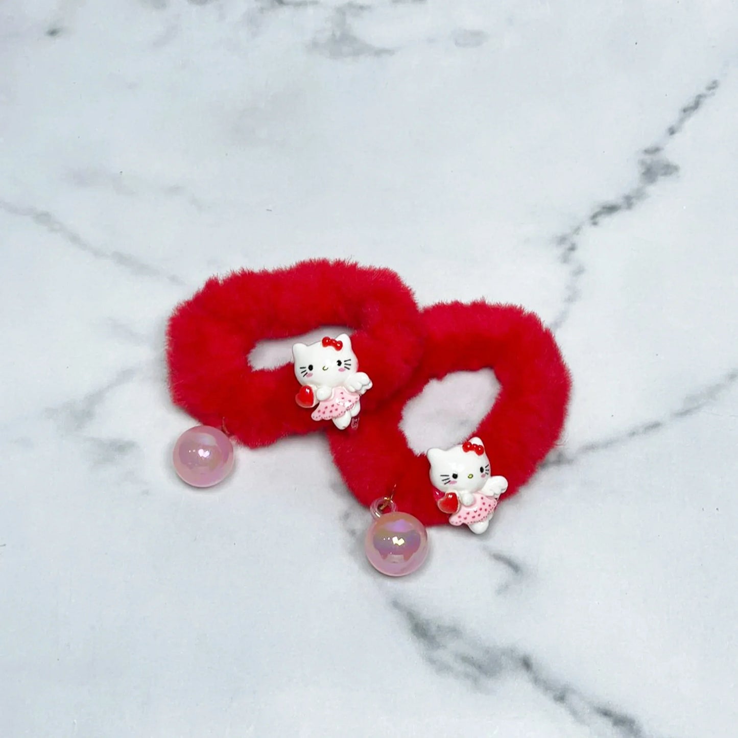 Red kids furry hair ties with cute white cat charms and pink beads on marble surface