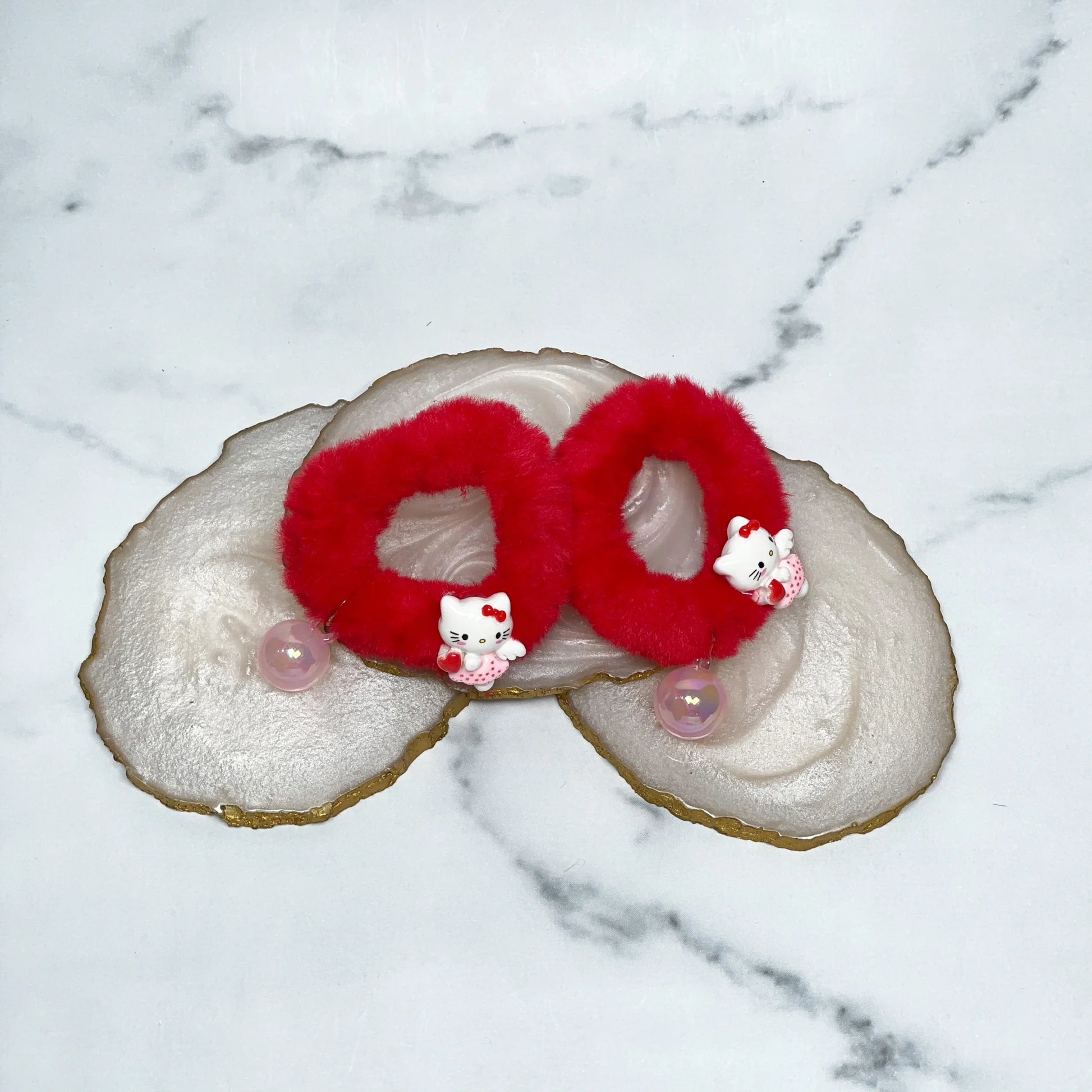 Red kids furry hair ties with cute white bear charms displayed on marble coasters
