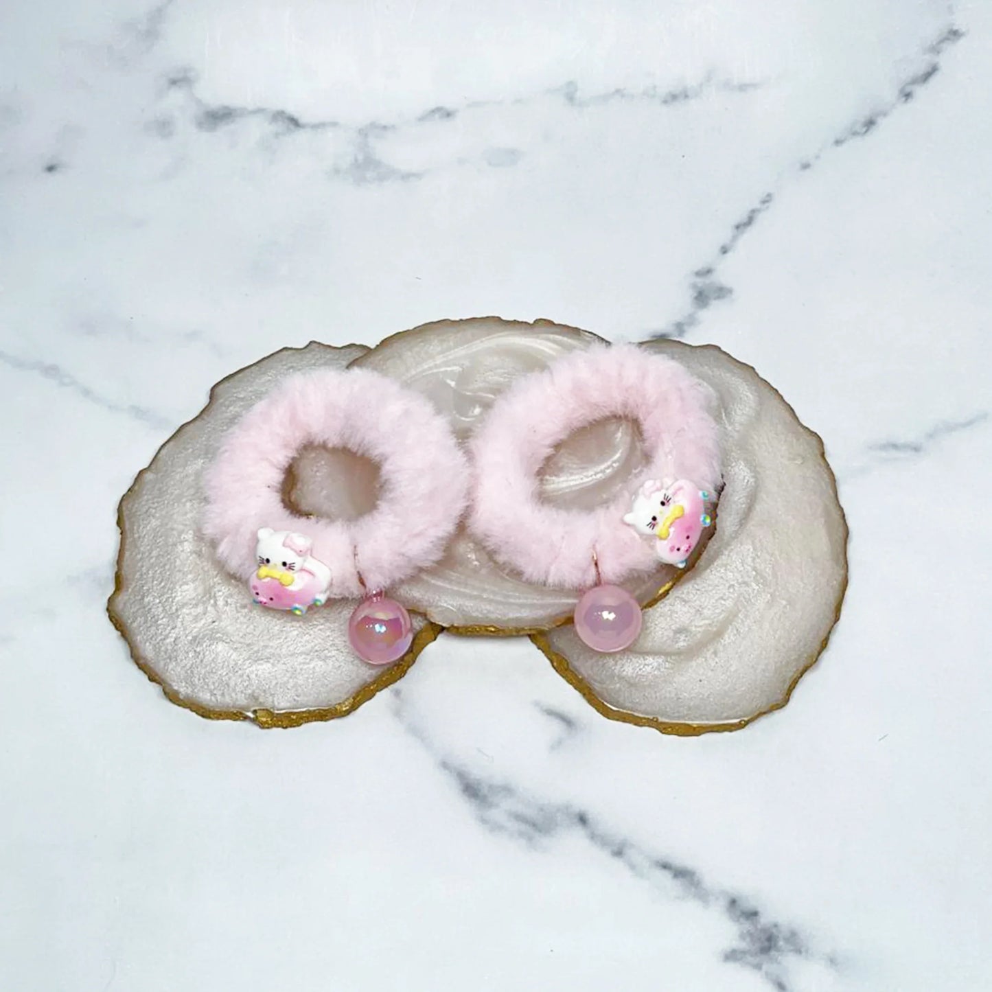 Pink kids furry hair ties with unicorn charms and beads placed on a decorative crystal plate