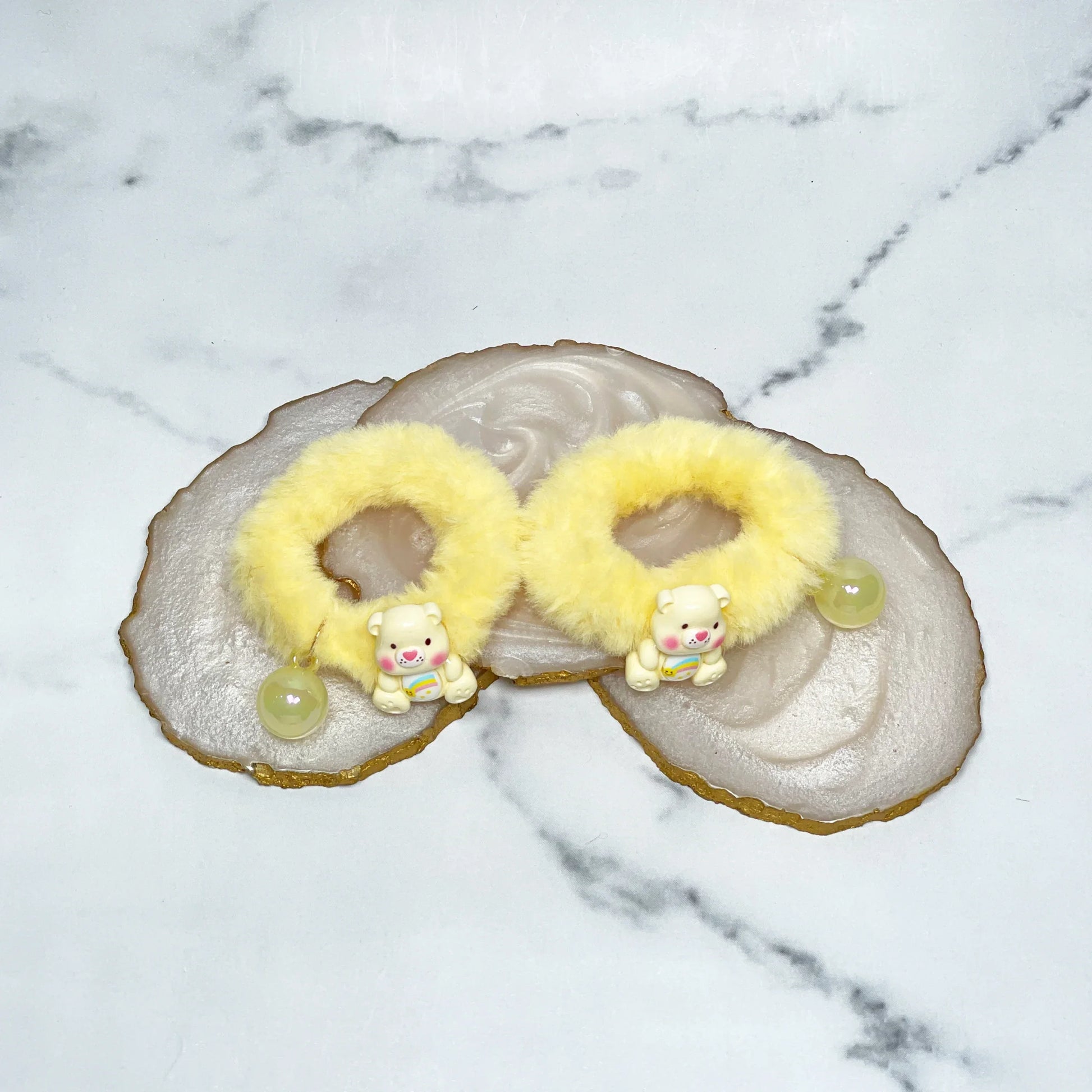 Yellow kids furry hair ties with cute bear charms and small beads on a marble surface