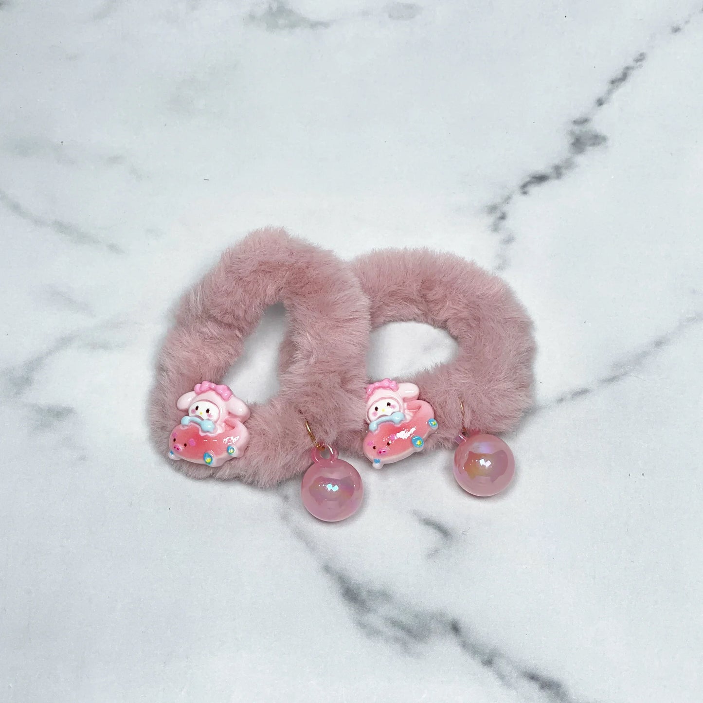 Pink kids furry hair ties with cute character and pink pearl charm on marble background
