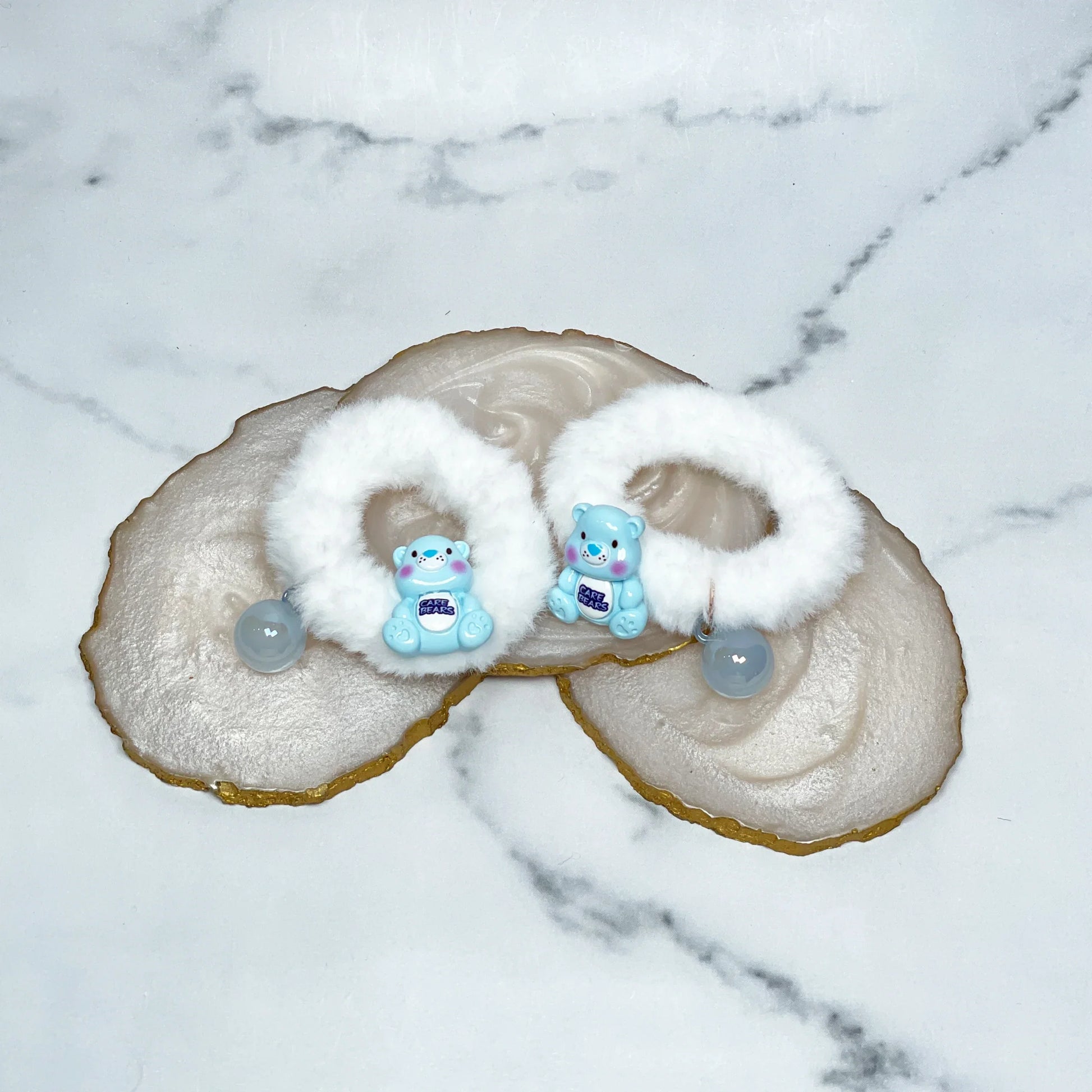 White kids furry hair ties with blue bear charms and beads on marble background