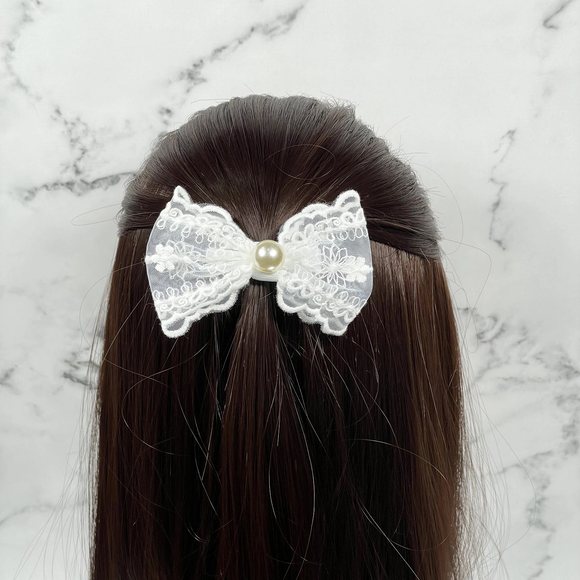 White lacy alligator bow clips with pearl center worn on dark brown hair against marble background