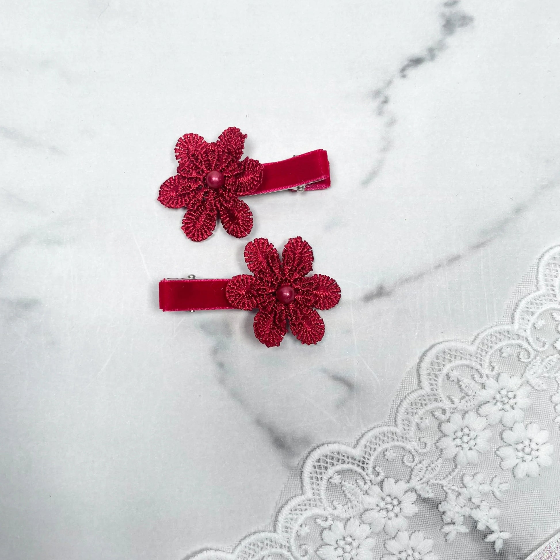 Pair of Lacy Flower Alligator Hair Pins with Beads in red on a marble surface with lace fabric