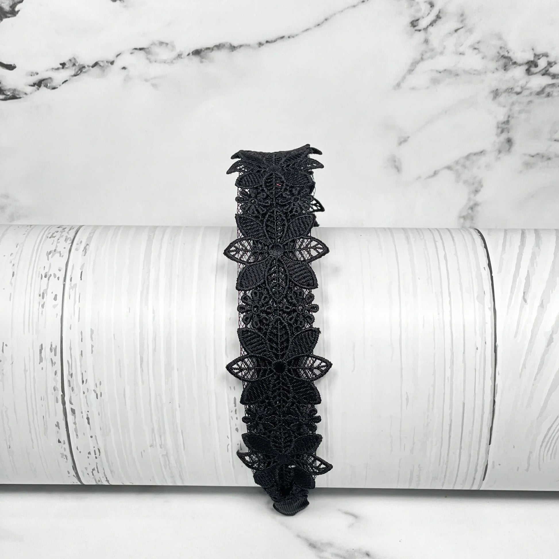 Black medium broad colored hair bands with intricate floral lace design on white wooden background