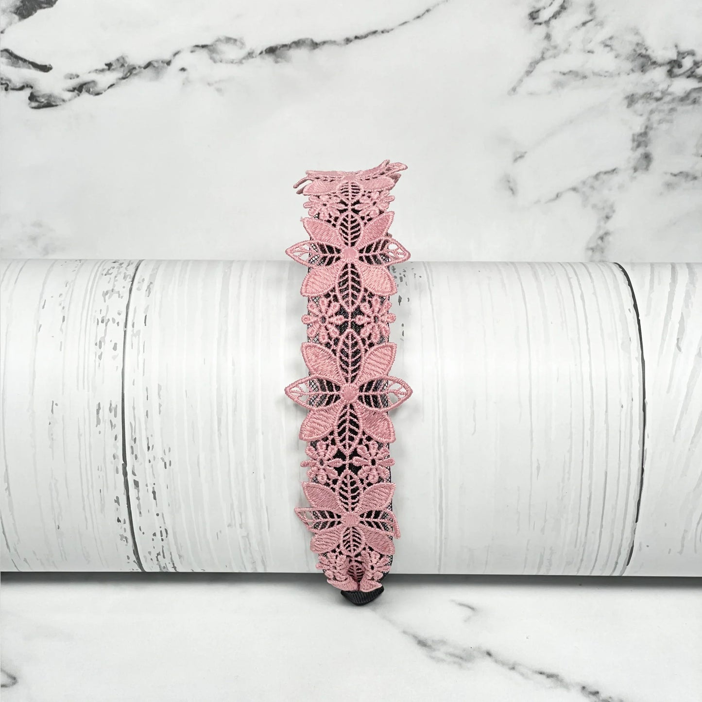 Medium broad colored hair bands in pink floral lace design displayed on white wooden surface