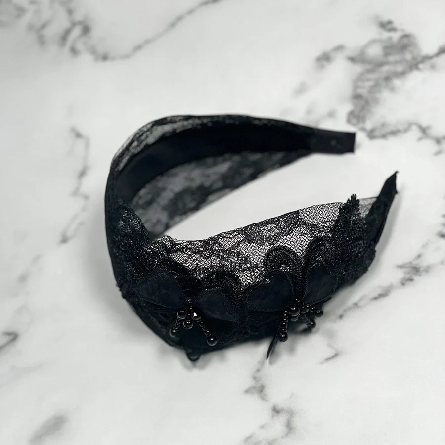 Black lace mesh broad hairband with floral design and bead embellishments on marble background