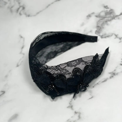 Black lace mesh broad hairband with floral design and bead embellishments on marble background