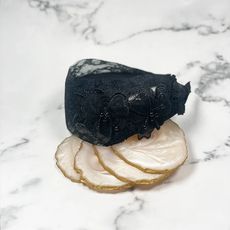Black mesh broad hairband with floral lace design displayed on white marble background