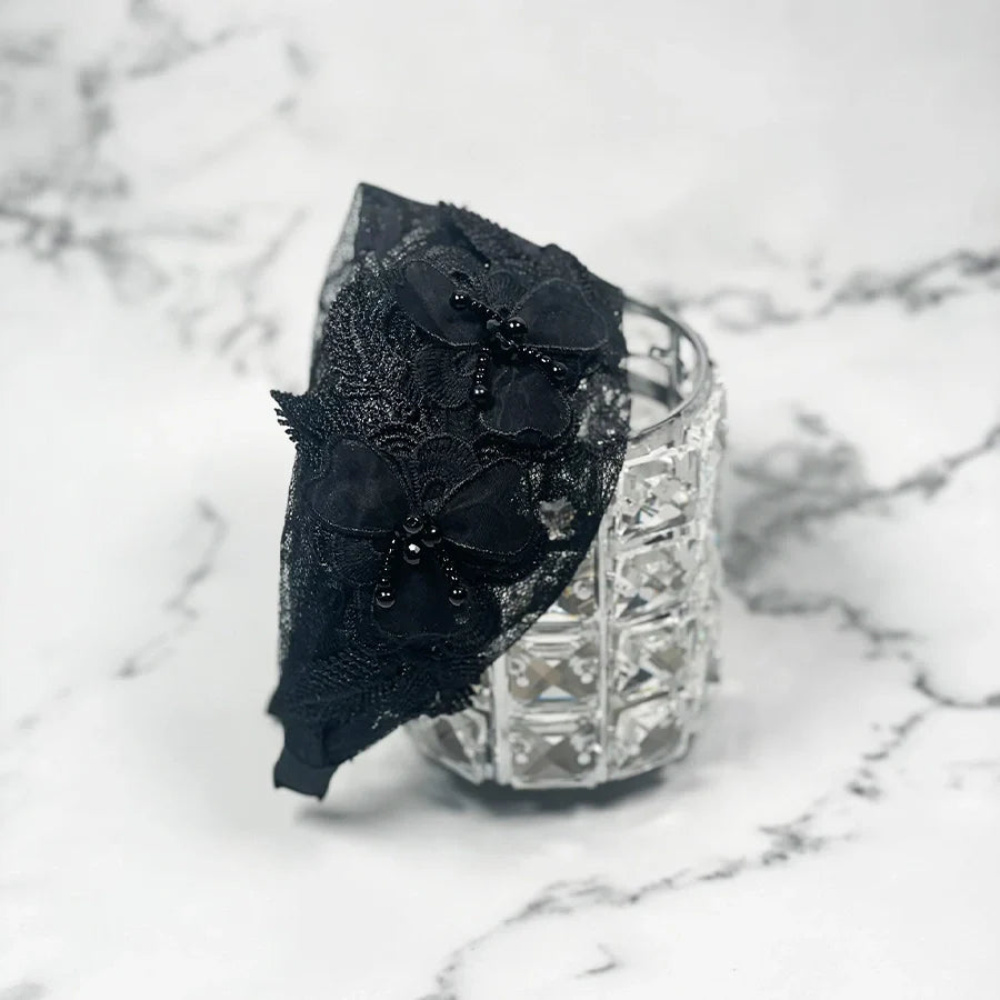 Black mesh broad hairband with floral lace and bead embellishments on a white marble background