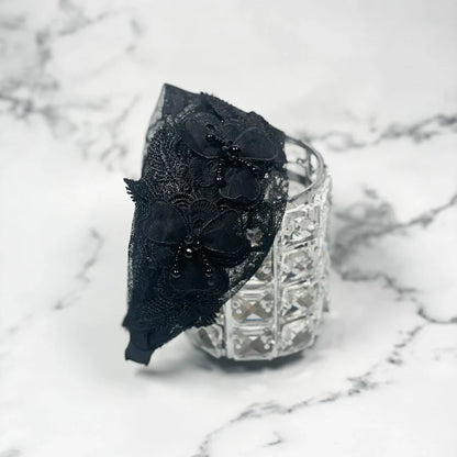 Black mesh broad hairband with floral lace and bead embellishments on a white marble background