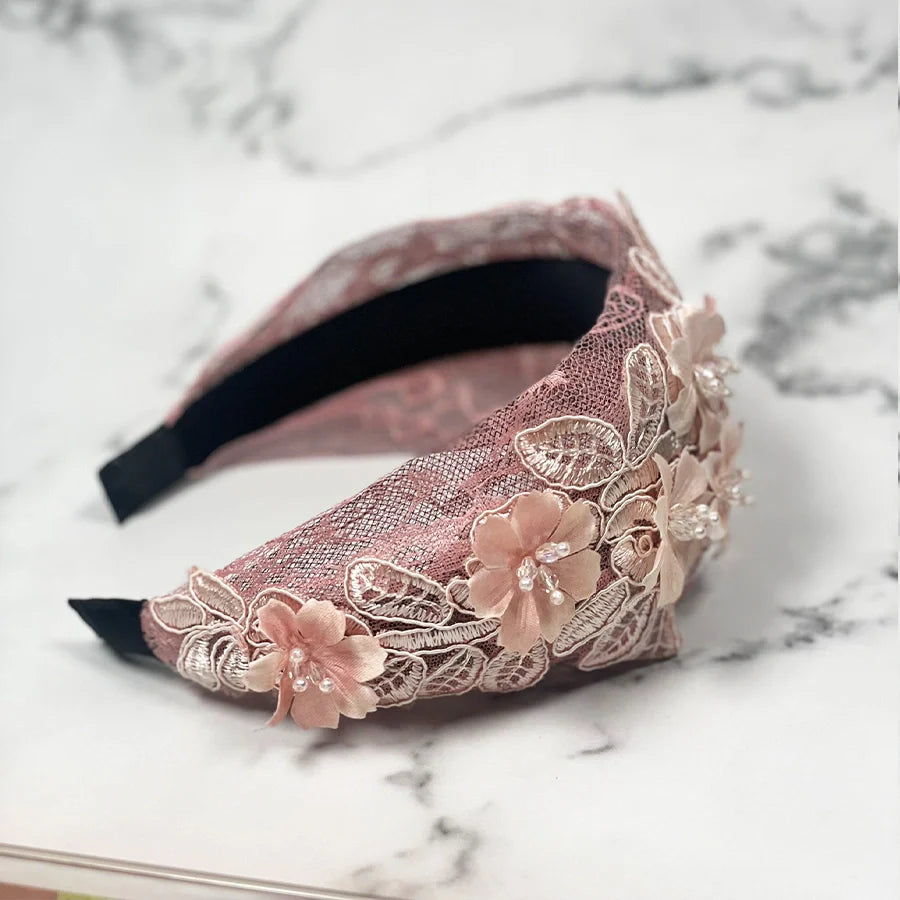 Pink mesh broad hairband with floral lace and bead embellishments on marble surface