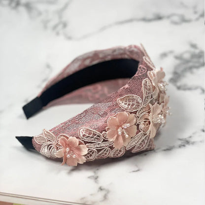 Pink mesh broad hairband with floral lace and bead embellishments on marble surface