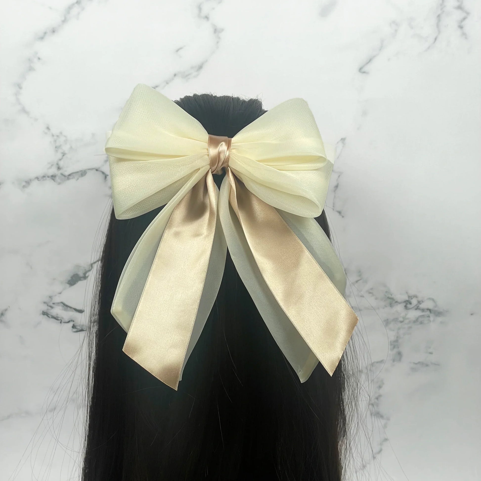 Cream colored Organza and Satin Bow Clips attached to black hair against a marble background