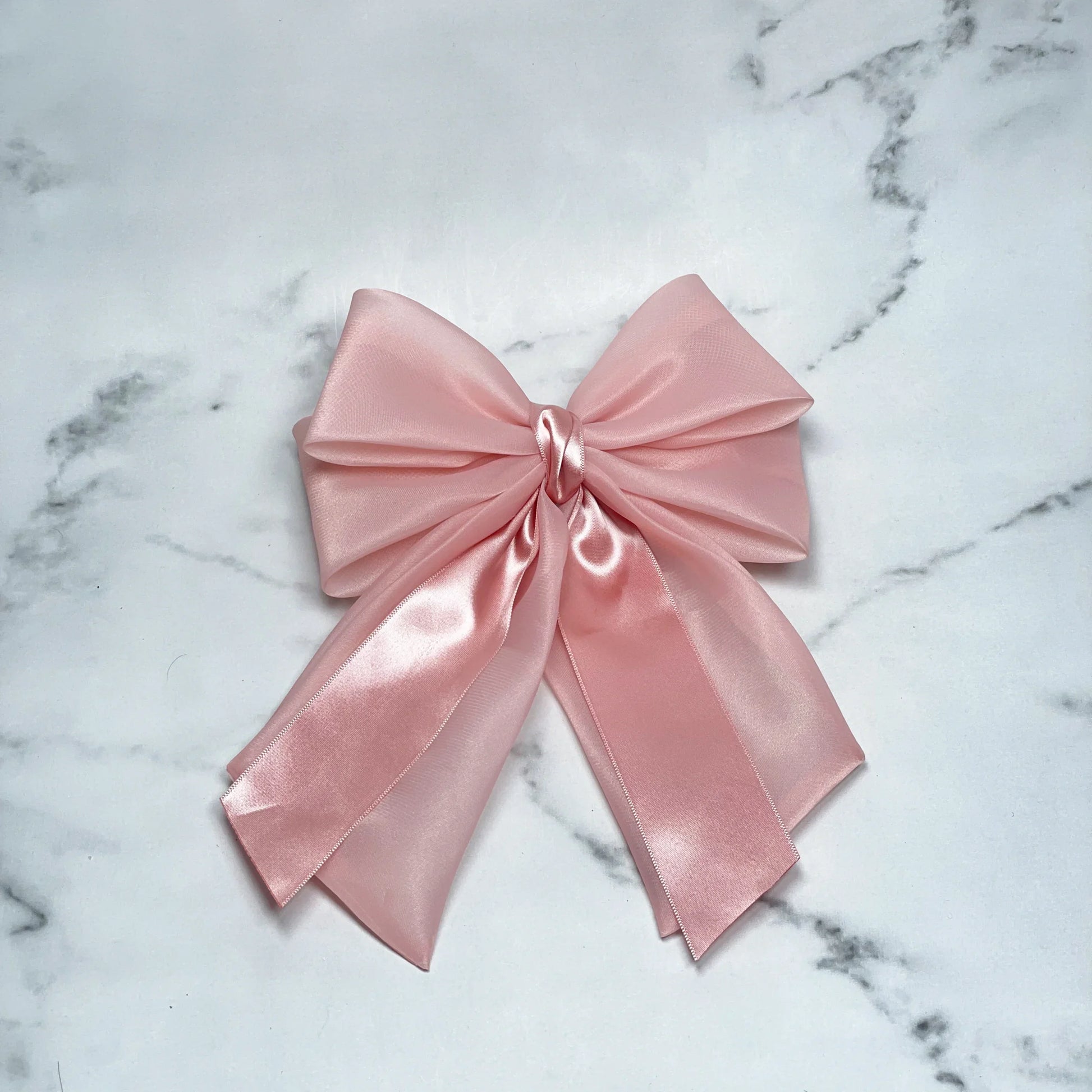 Pink Organza and Satin Bow Clips with a smooth, shiny finish laid on a marble surface