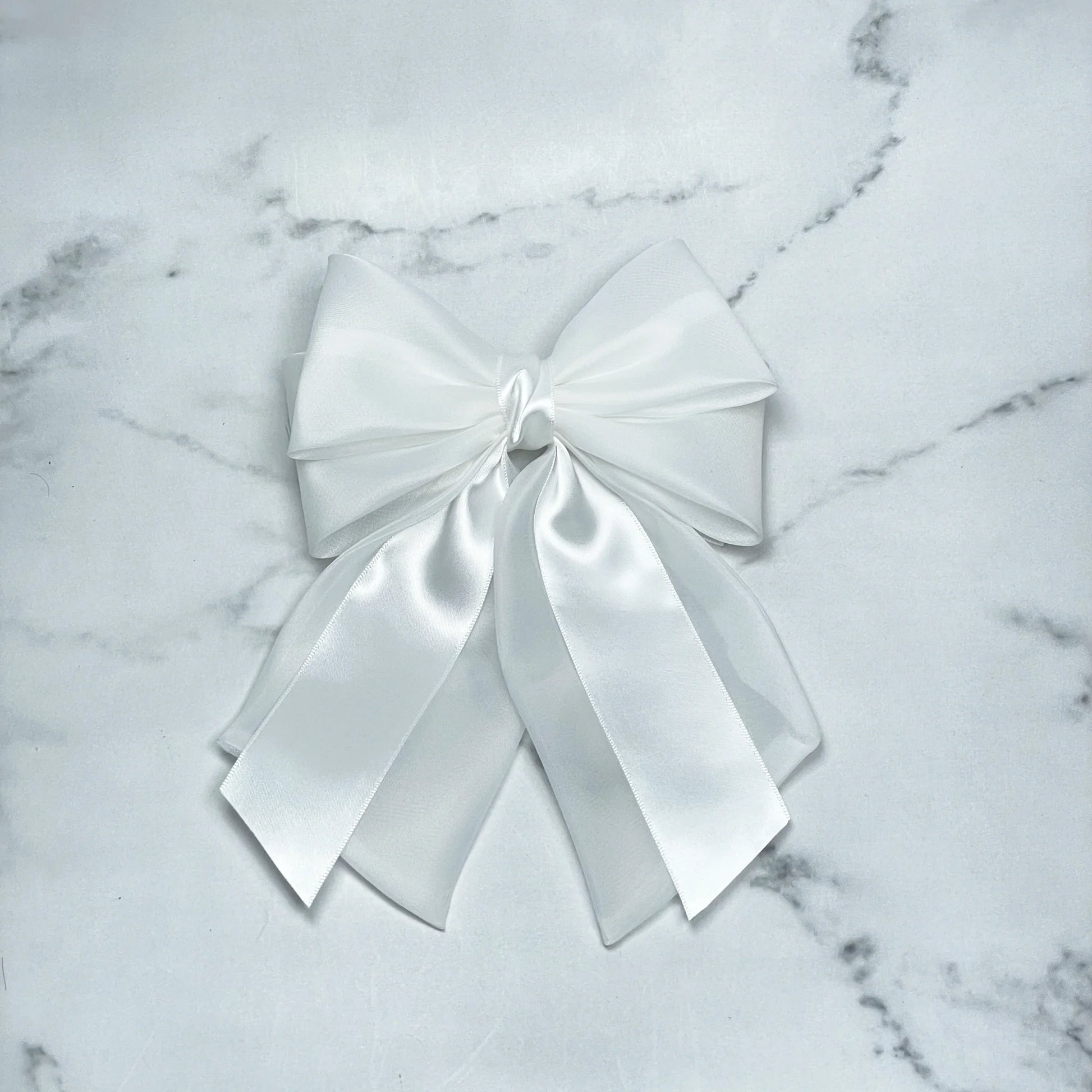 White organza and satin bow clips with layered ribbons on a marble background
