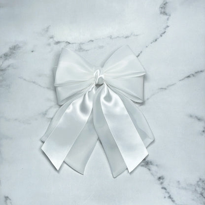 White organza and satin bow clips with layered ribbons on a marble background