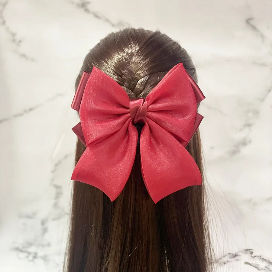 Red organza satin bow hair clips styled on back of dark brown hair with marble background