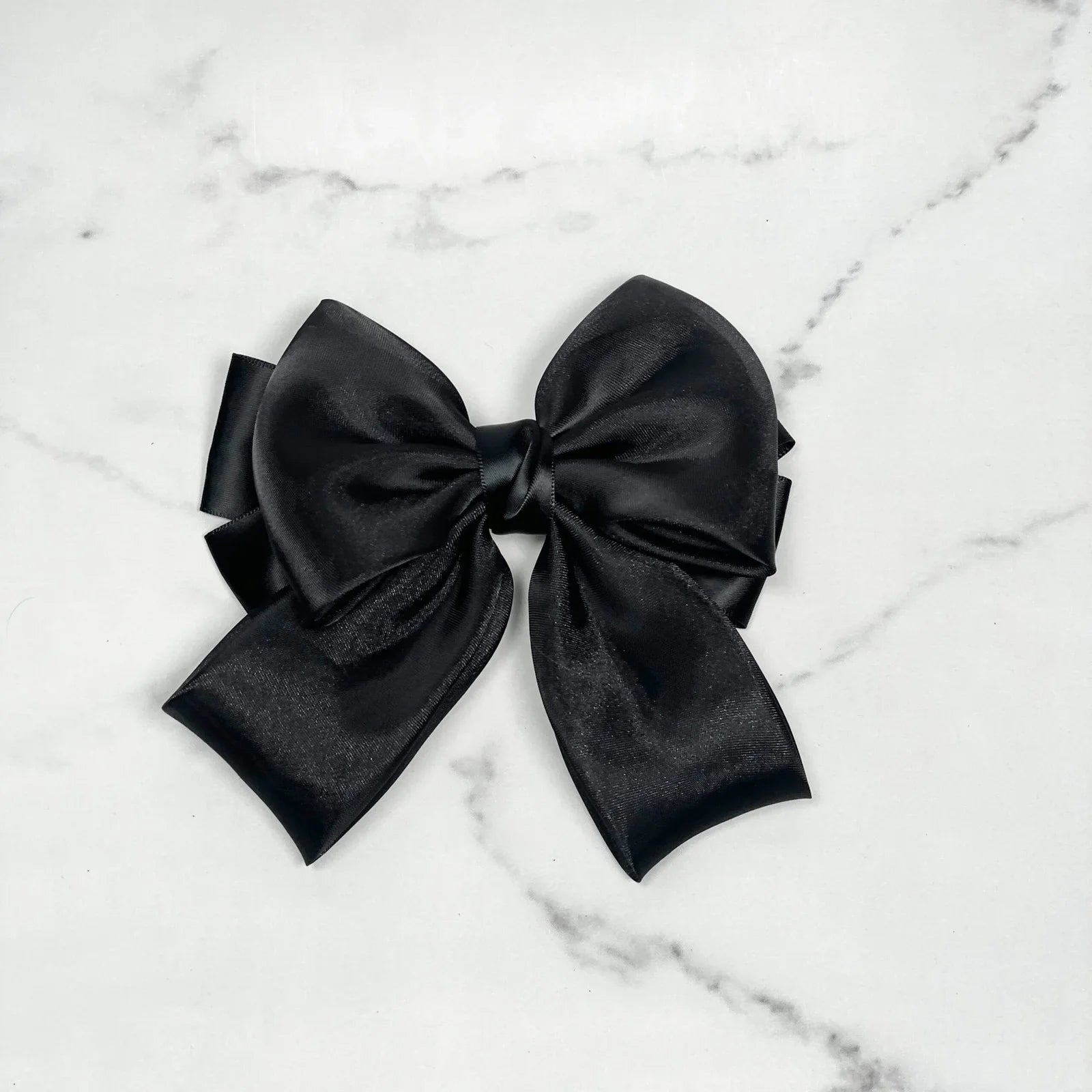 Black organza satin bow hair clips with a smooth shiny finish on a white marble background