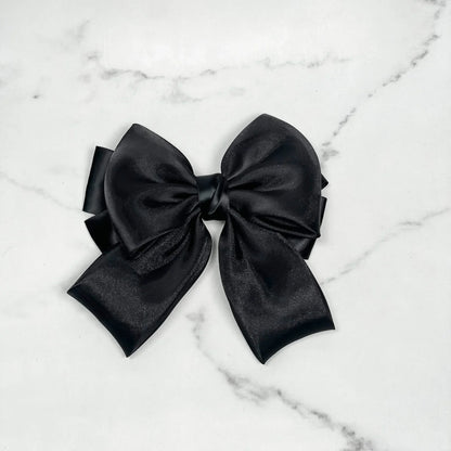 Black organza satin bow hair clips with a smooth shiny finish on a white marble background
