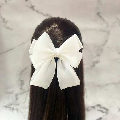 White organza satin bow hair clips styled on long dark hair against marble background