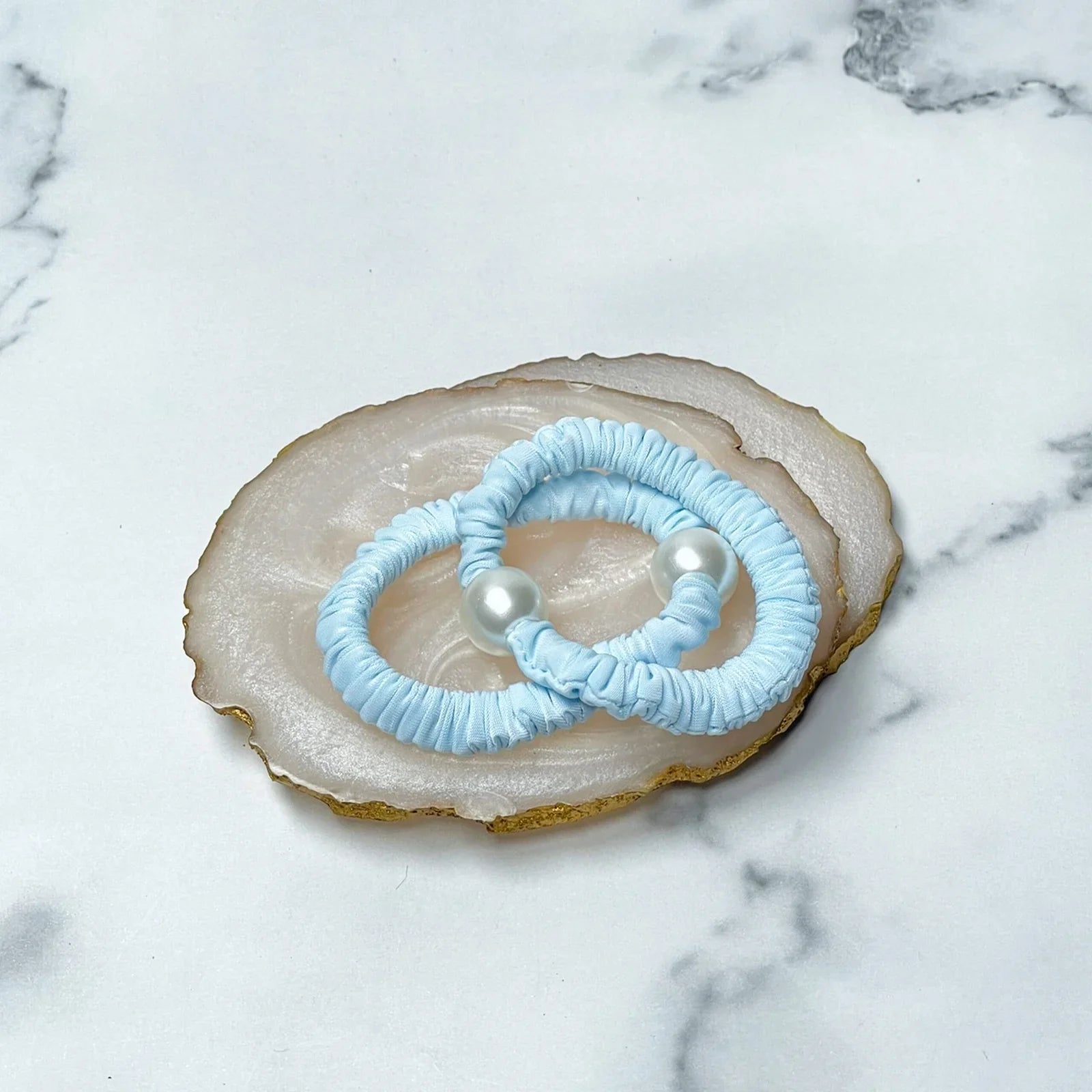 Pastel hair ties with pearl in light blue placed on a decorative agate slice on white marble