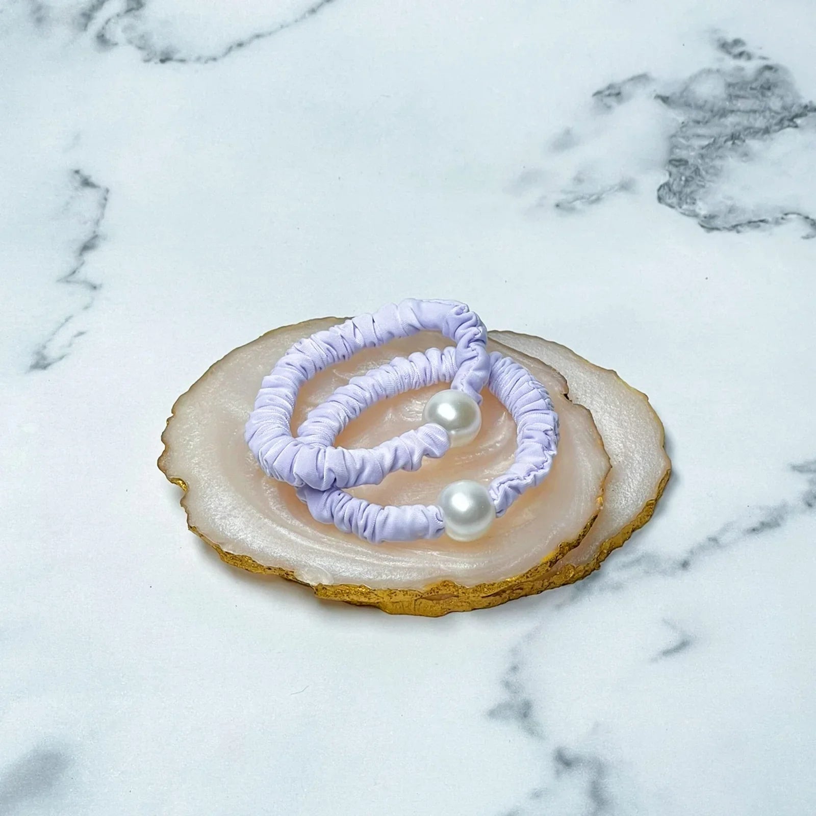 Pastel hair ties with pearl detail displayed on an agate slice on marble background