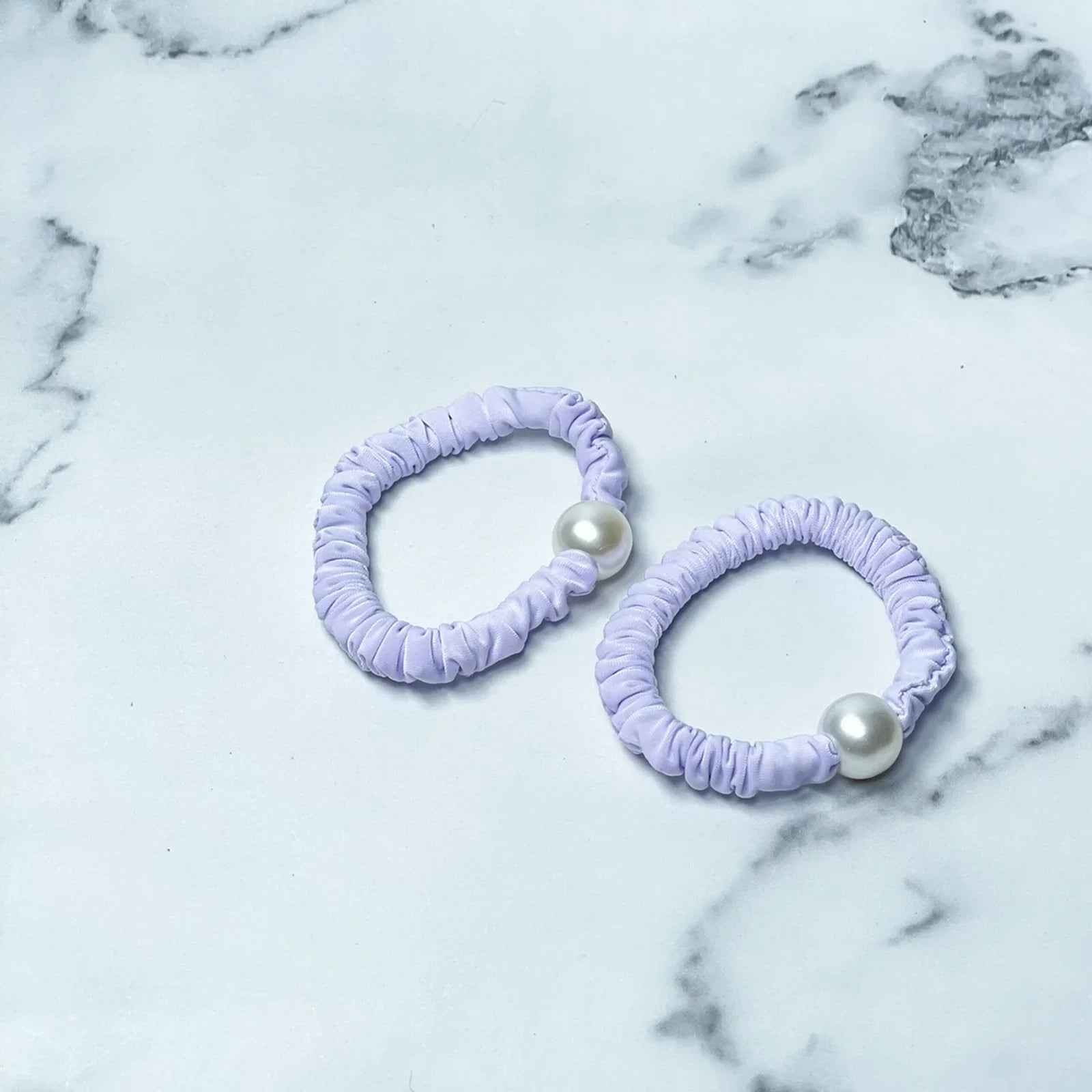 Pastel hair ties with pearl detail in light purple on a marble background