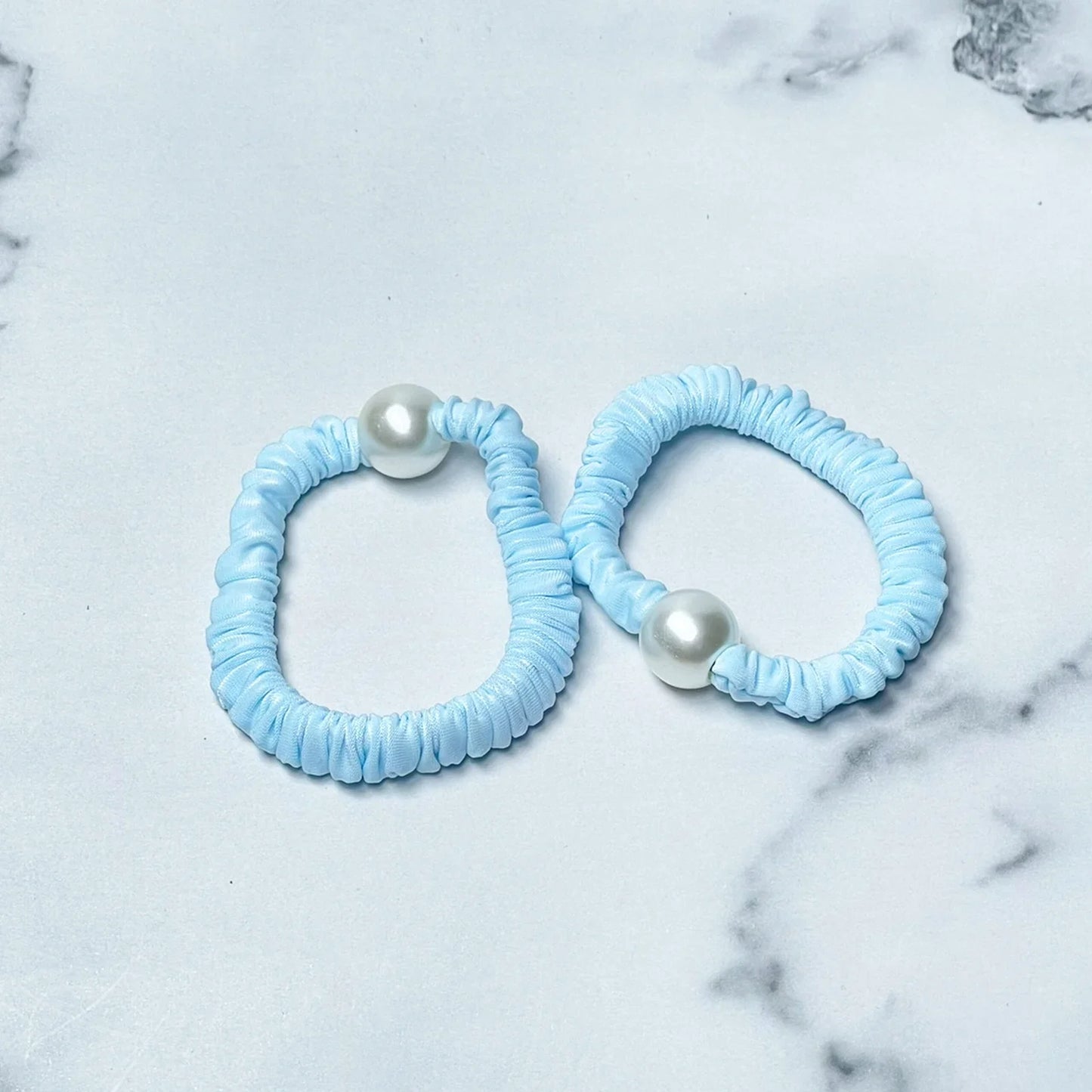 Two pastel hair ties with pearl in light blue color on a marble surface