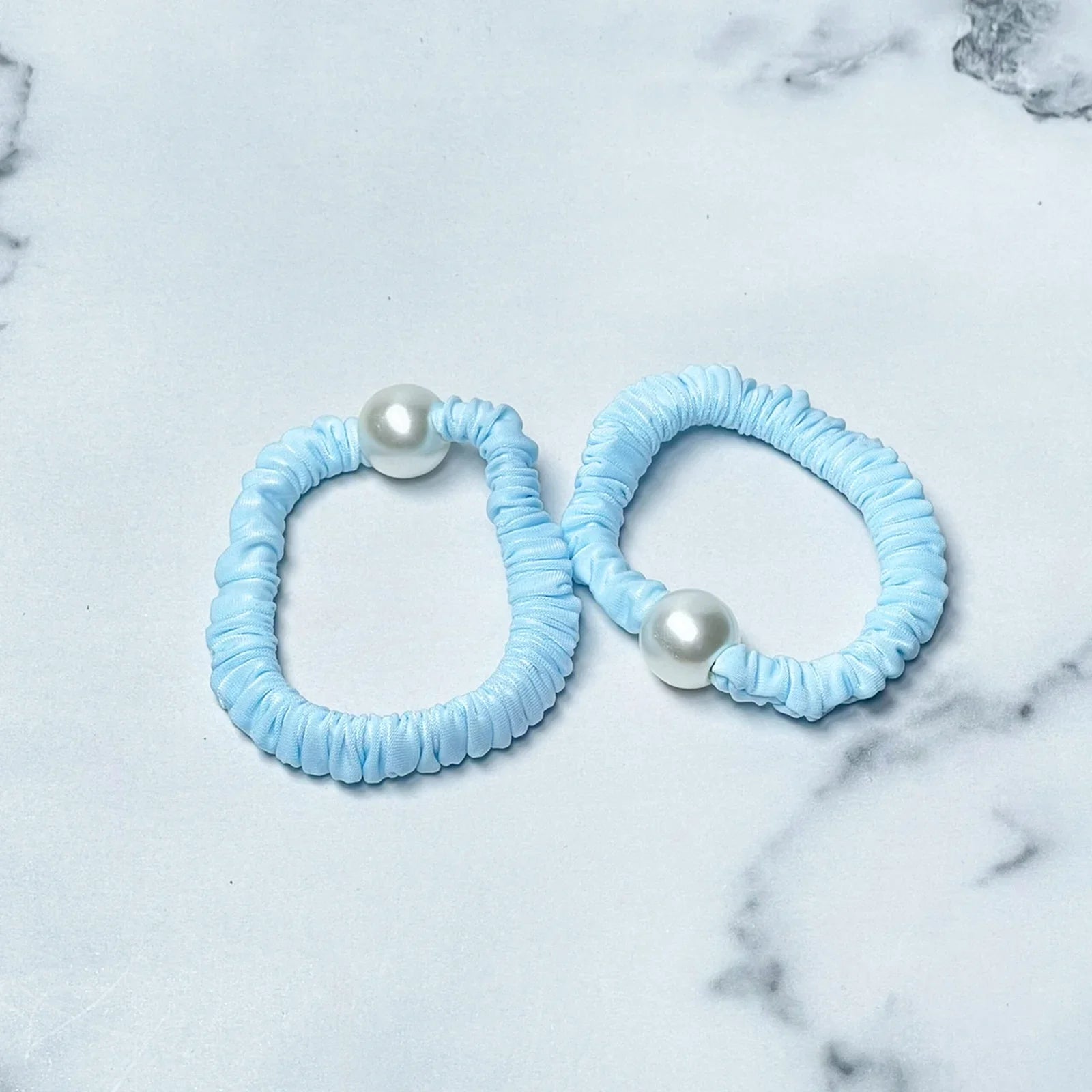 Two pastel hair ties with pearl in light blue color on a marble surface