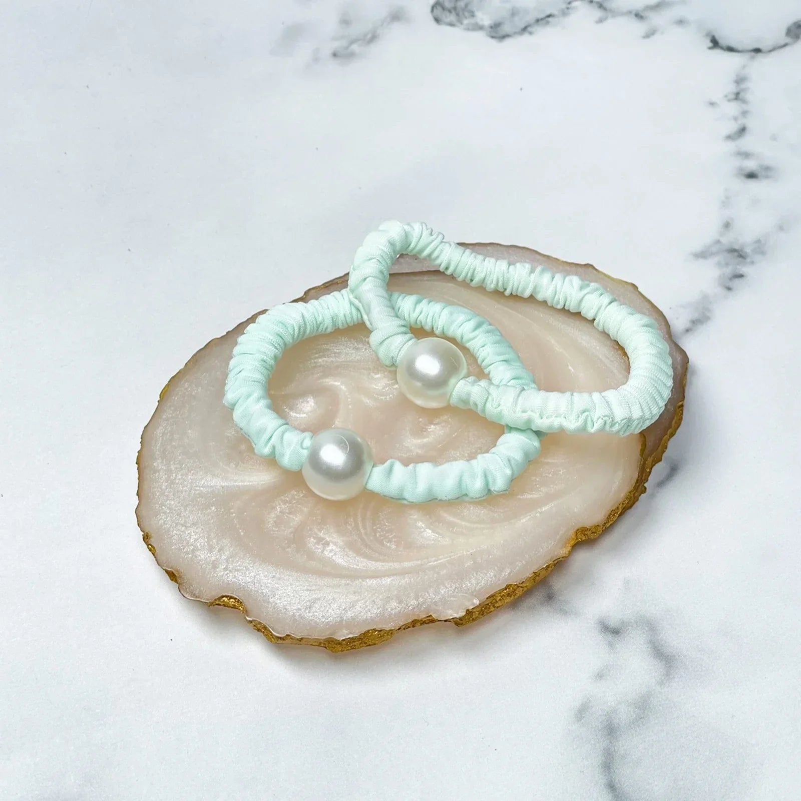 Pastel hair ties with pearl detail in light blue displayed on a decorative shell dish