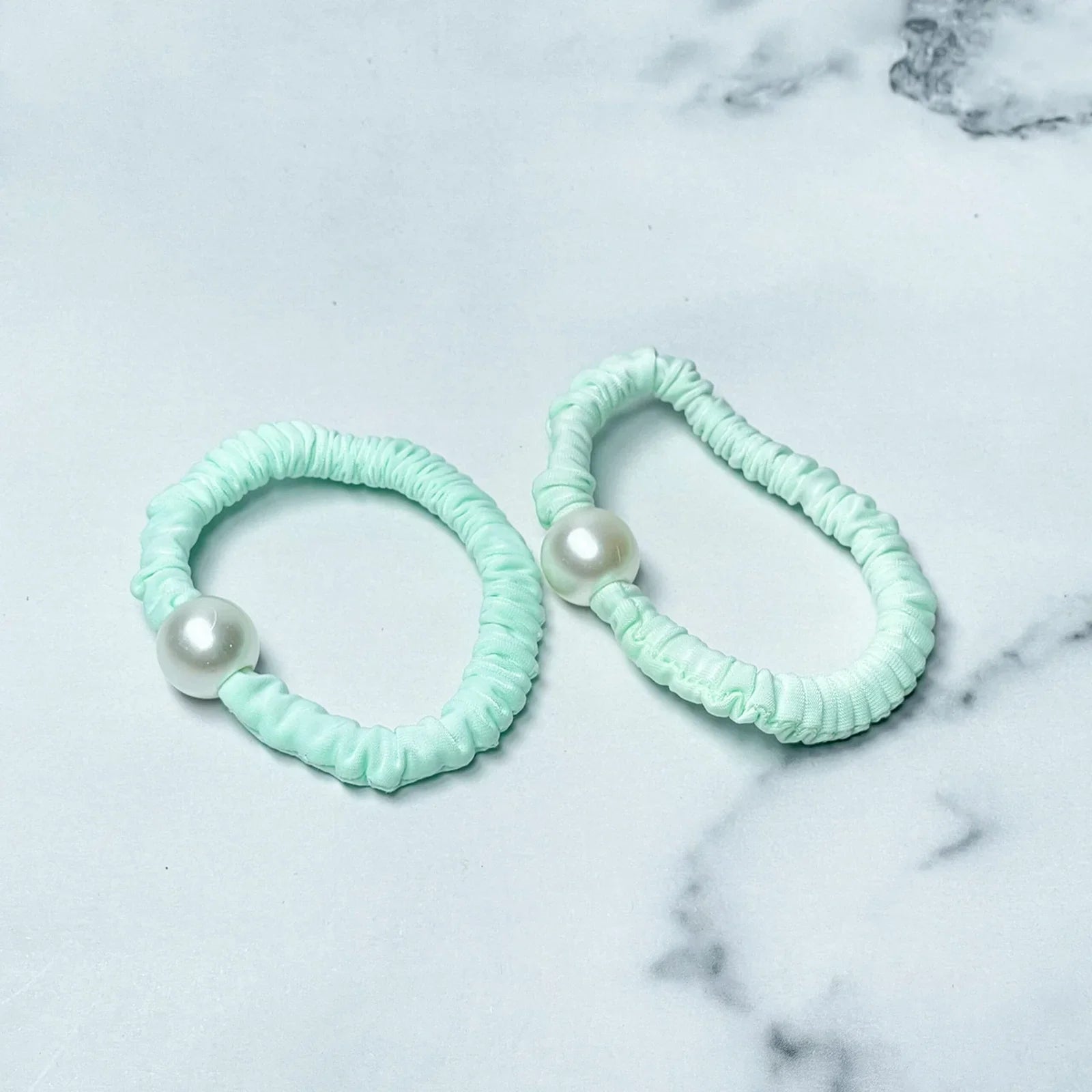 Pastel hair ties with pearl decoration in light mint green on a marble surface
