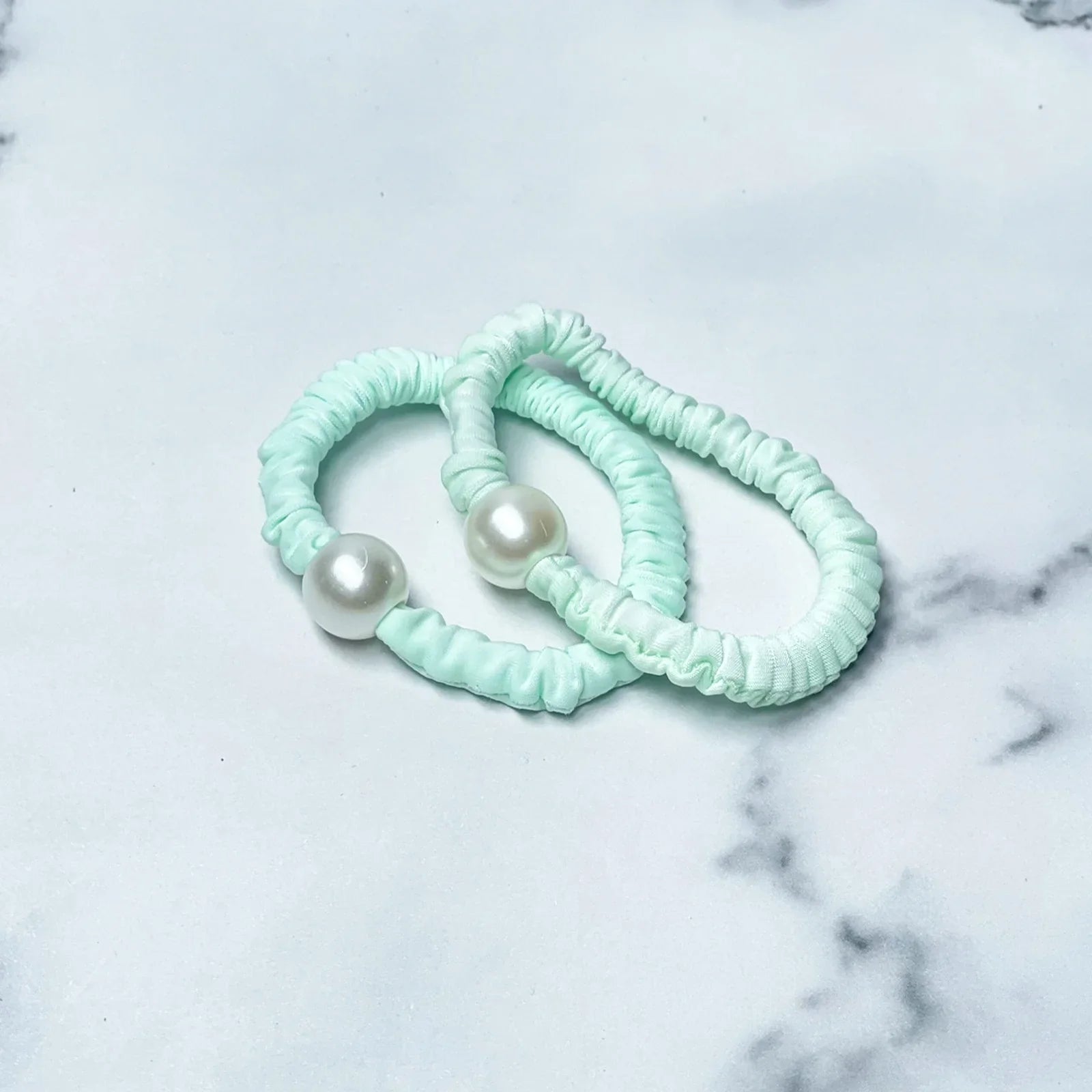 Pastel hair ties with pearl in soft mint green color on a marble background