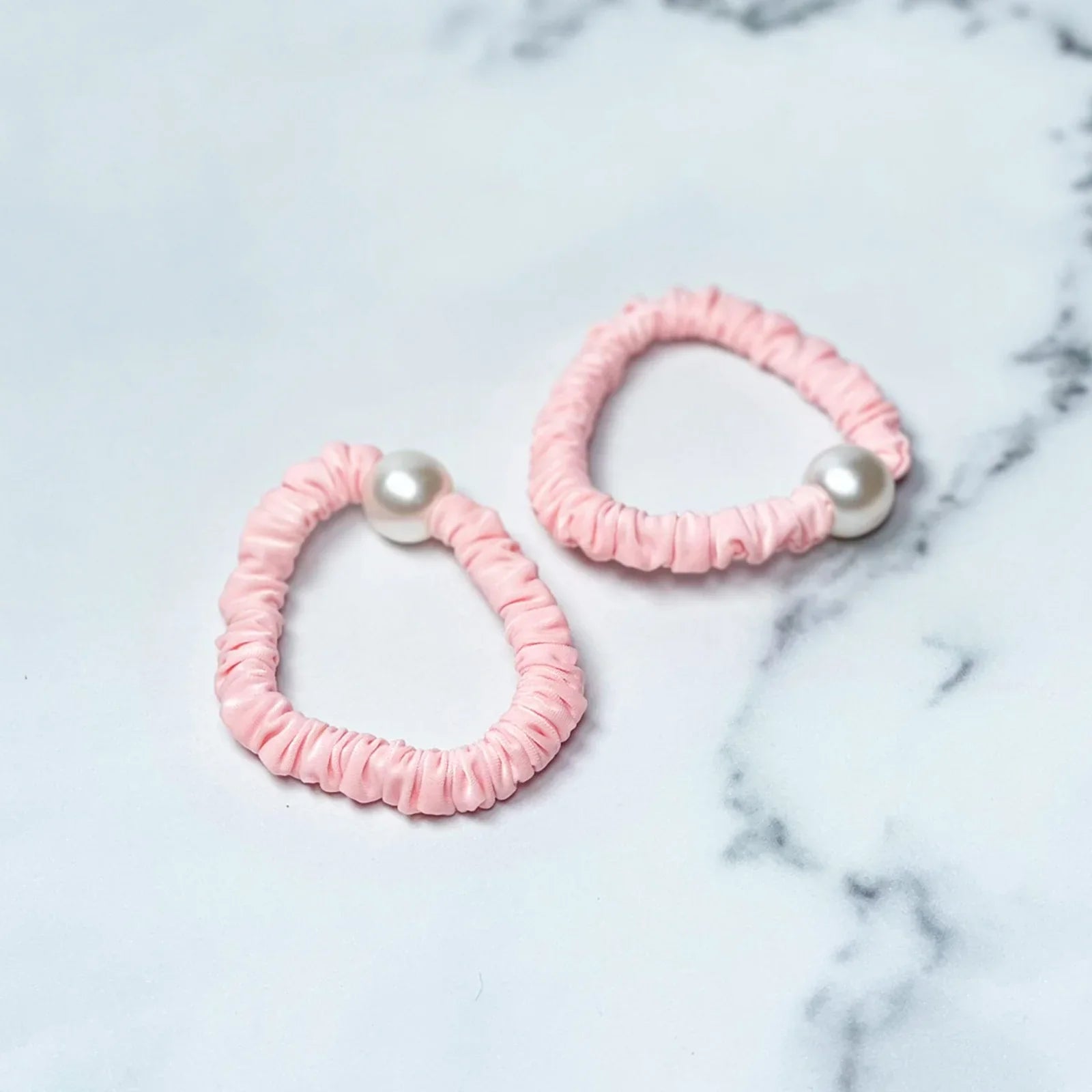 Pink pastel hair ties with pearl detail on a marble surface for stylish hair accessories