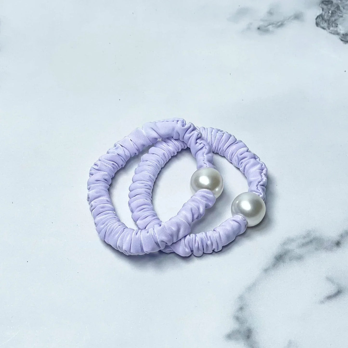 Pastel hair ties with pearl detail in soft lavender color on marble background