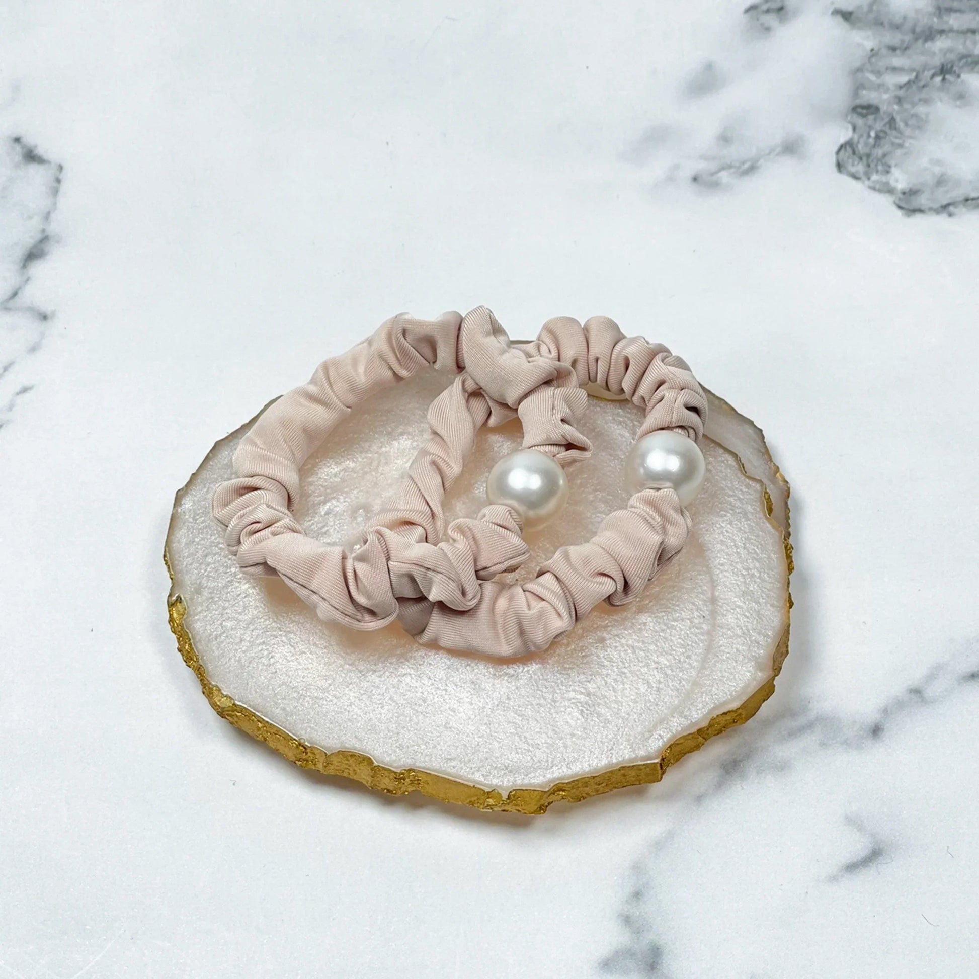 Beige scrunchie pearl hair ties with large white pearls on marble background