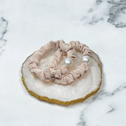Beige scrunchie pearl hair ties with large white pearls on marble background