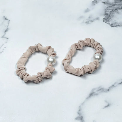 Beige fabric scrunchies with single pearl accents pearl hair ties on marble background