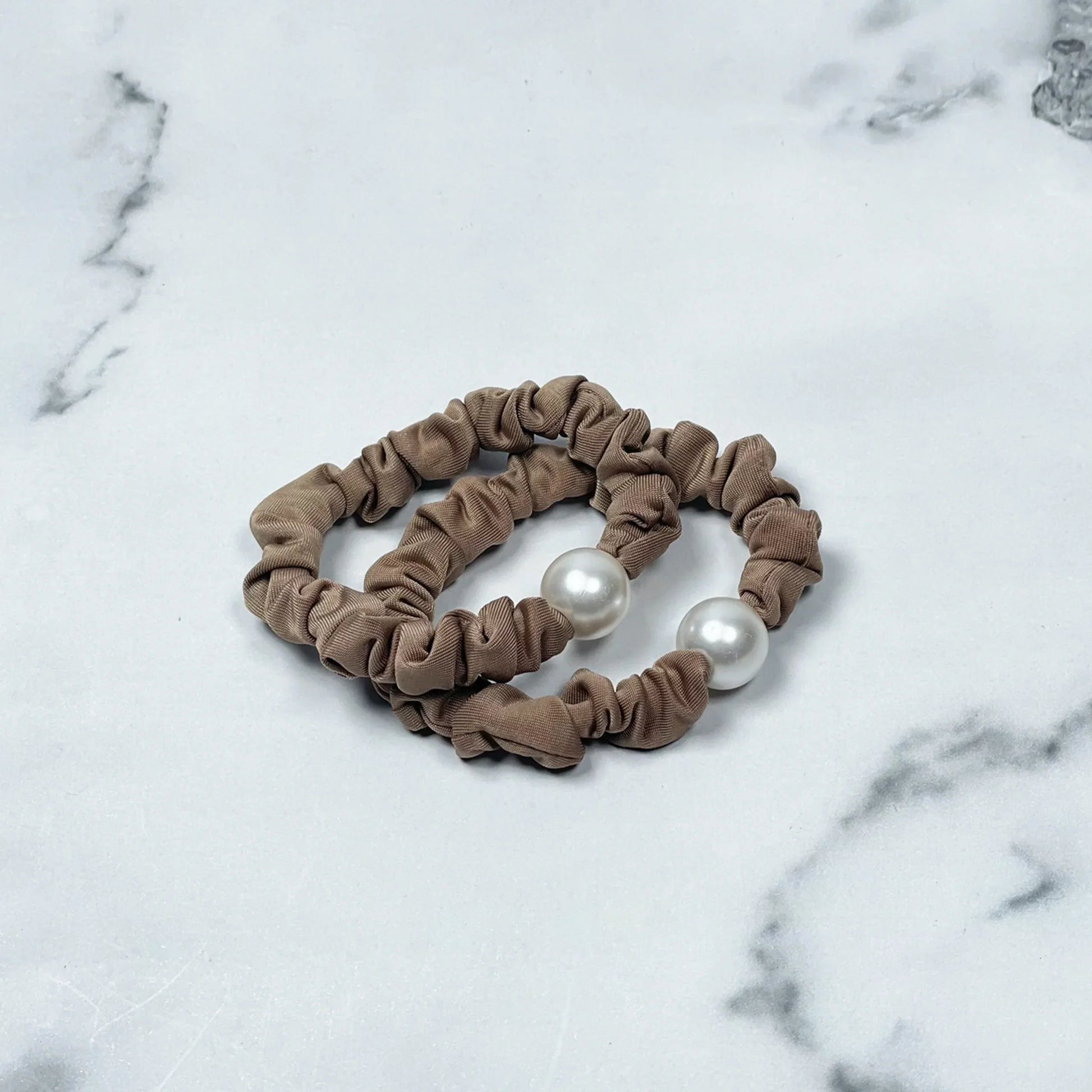 Brown fabric pearl hair ties with large white pearls on a marble surface