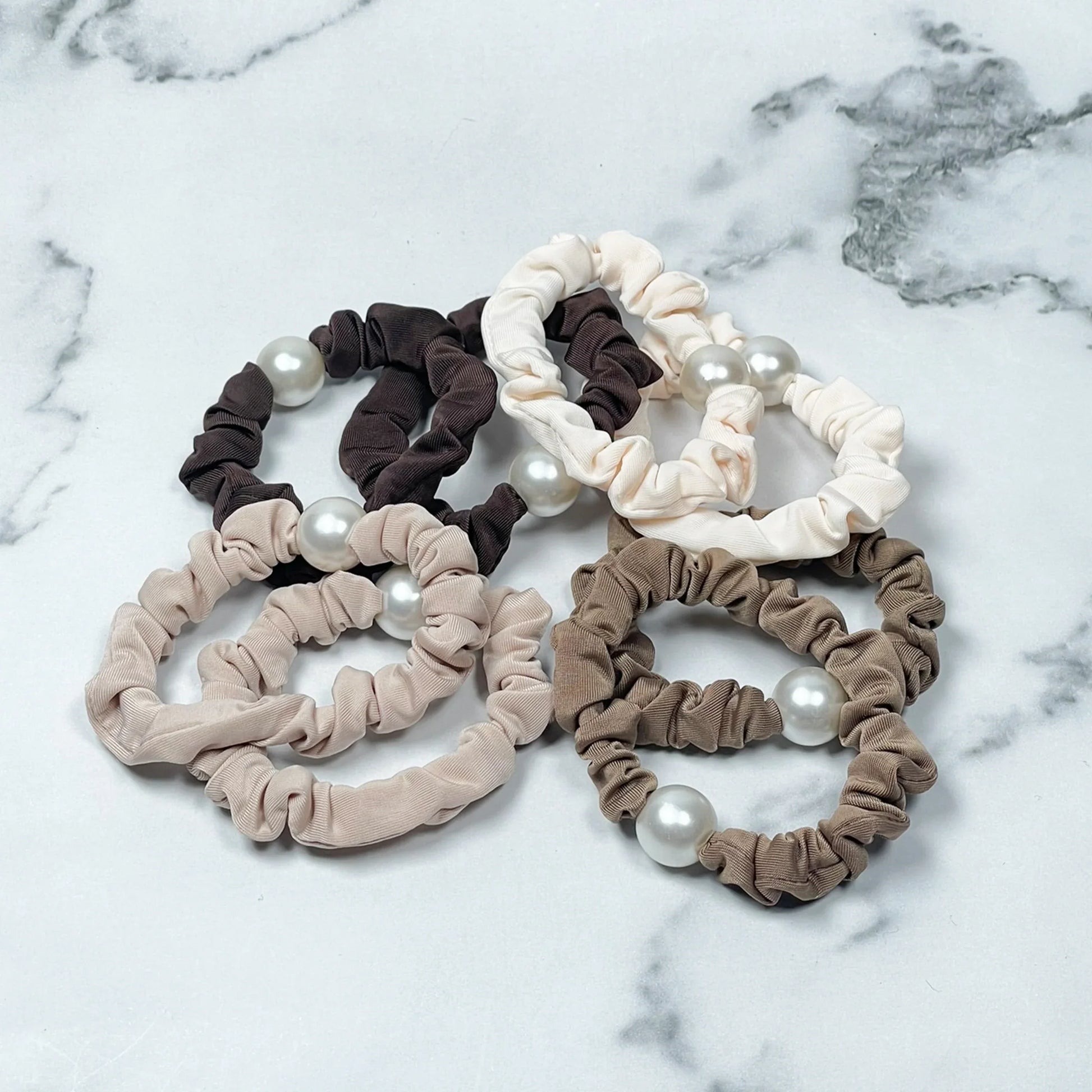 Set of pearl hair ties in neutral shades including beige, brown, and cream on marble background