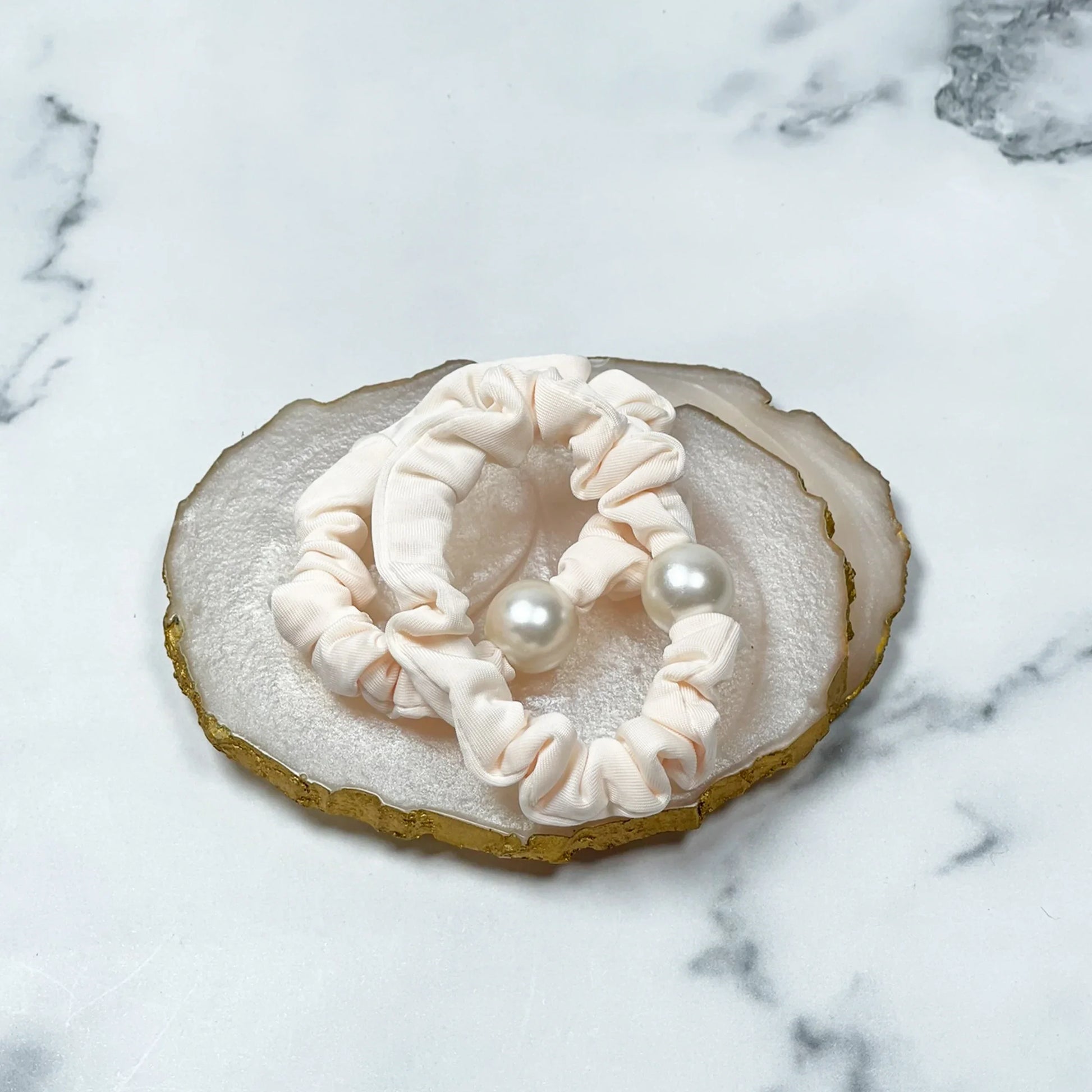 Cream fabric pearl hair ties with large white pearls placed on decorative agate slice