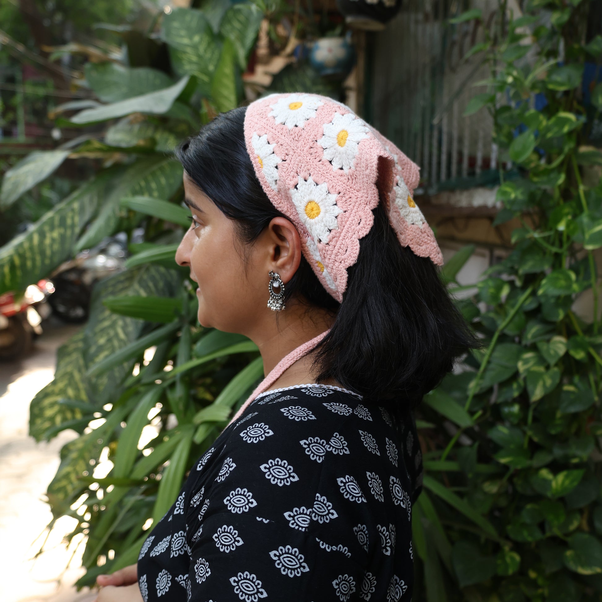 Bella Luxe pink crochet bandana with white daisy patterns worn by woman outdoors with black hair