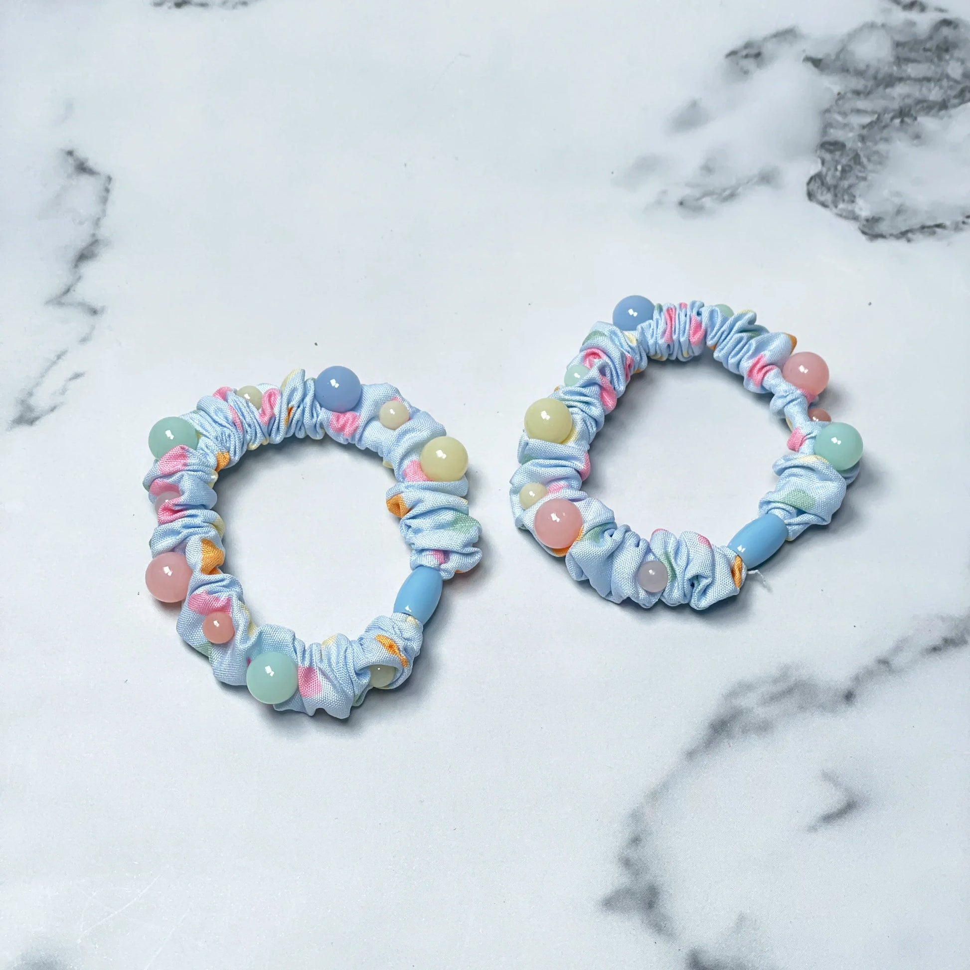 Set of printed hair ties with pastel beads on light blue elastic bands on marble surface