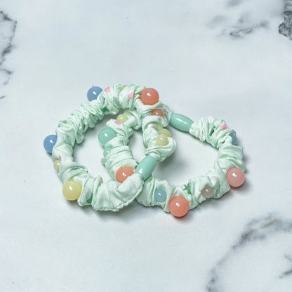 Light green printed hair ties with colorful bead accents on white marble surface