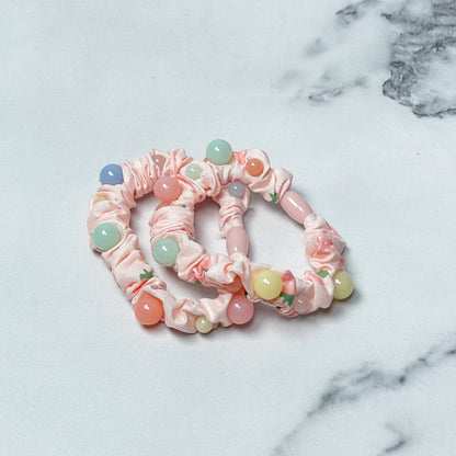 Pink printed hair ties with colorful beads laid on white and gray marble surface