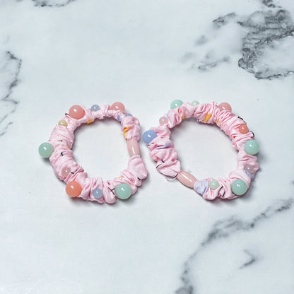 Pink printed hair ties with colorful beads displayed on a white marble surface