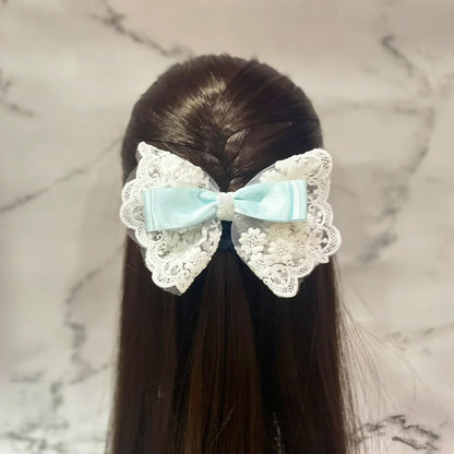 Satin bow clip with lace in light blue and white worn on dark brown hair styled in a half-up braid