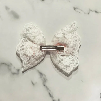 White satin bow clip with lace featuring delicate floral patterns on a metal clip