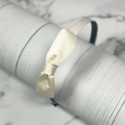 Elegant cream satin bow hairbands displayed on a white textured surface for stylish hair accessories